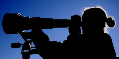 Silhouetted person looking through a telescope